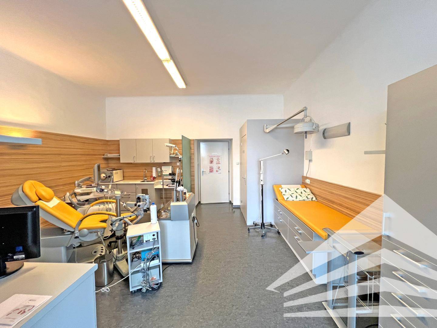 Behandlungszimmer mit medizinischer Ausstattung, Liege und Schränken.