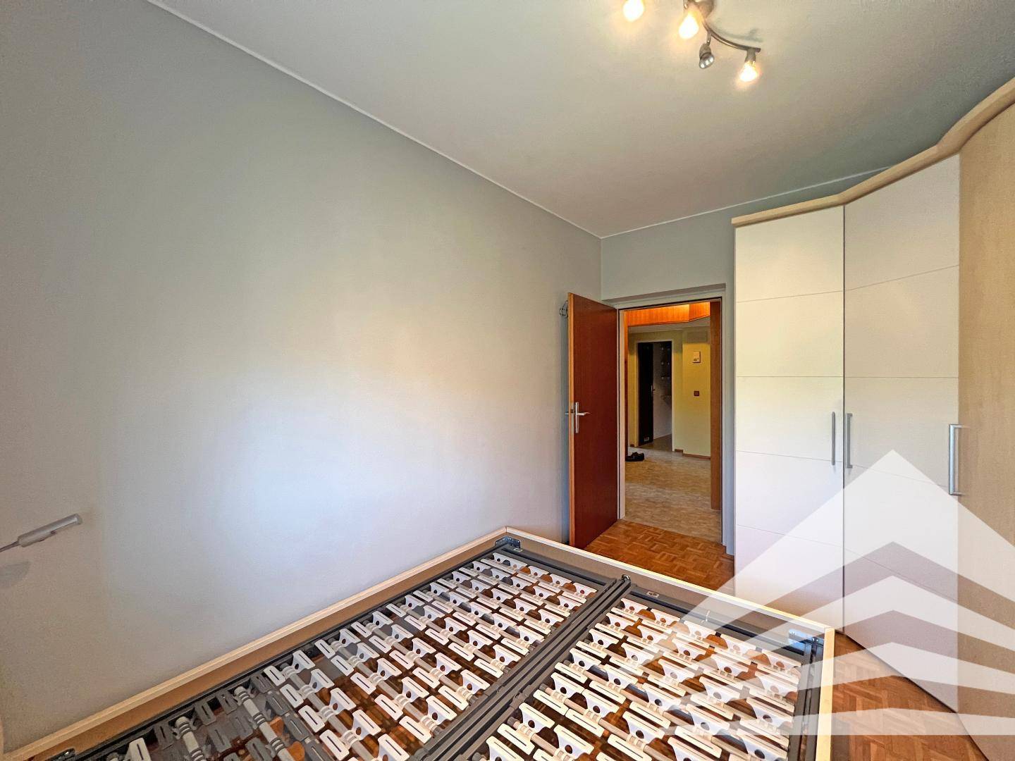 Schlafzimmer mit Bettgestell und Einbauschrank, Zugang zu einem weiteren Raum.