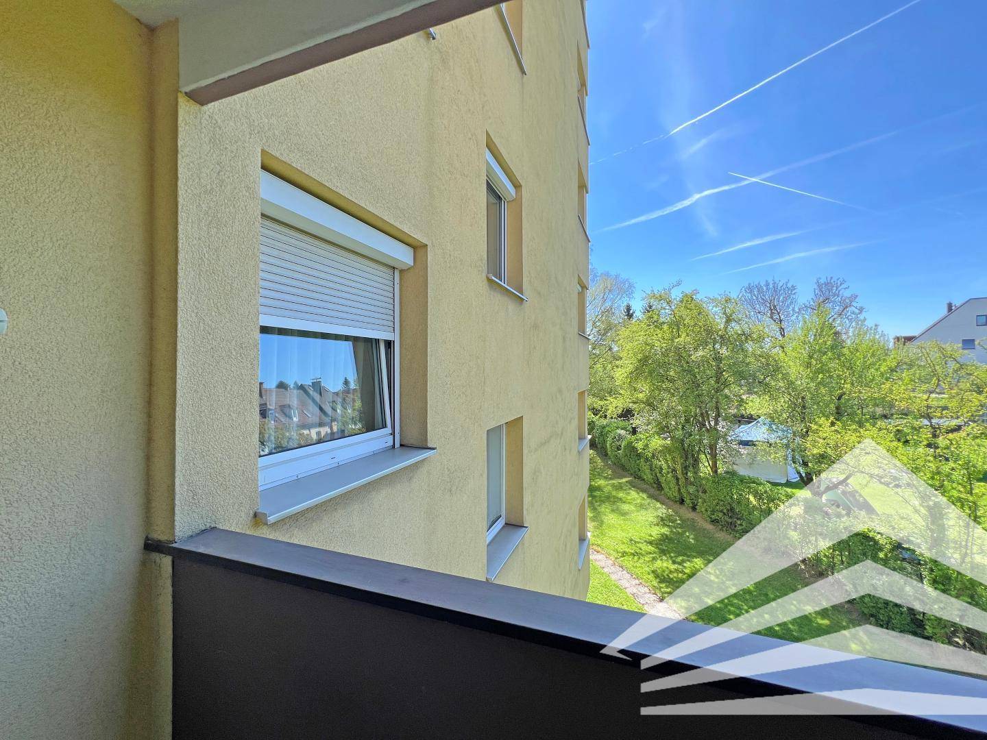 Blick vom Balkon auf eine grüne Gartenanlage und umliegende Gebäude.