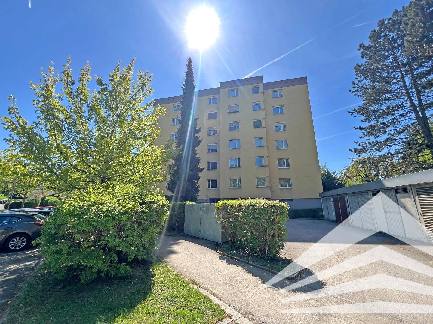 Mehrfamilienhaus mit gelber Fassade, umgeben von Bäumen und Parkplätzen.