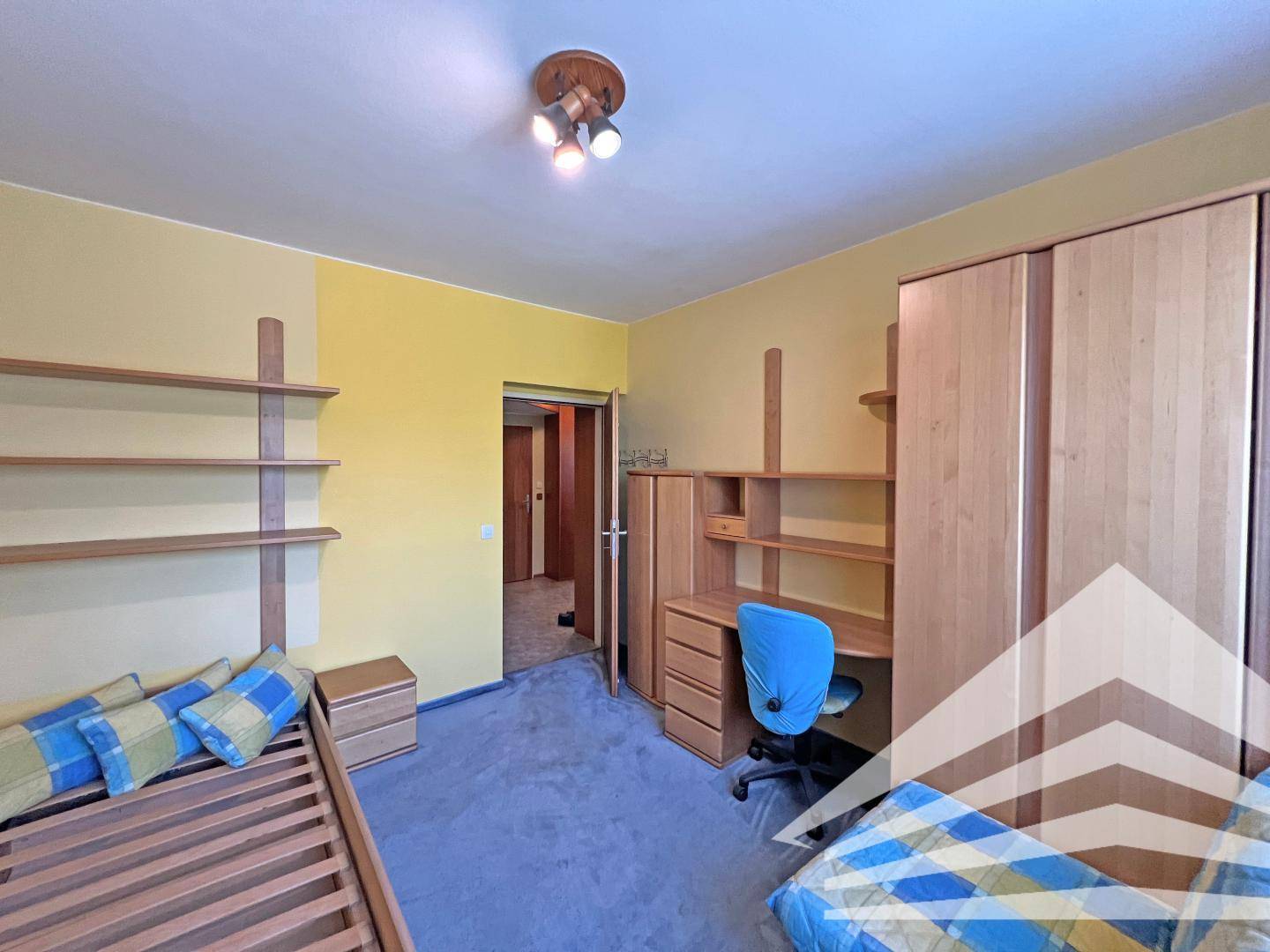 Schlafzimmer mit Bett, Schreibtisch und Regalen, in freundlichem Gelb gehalten.