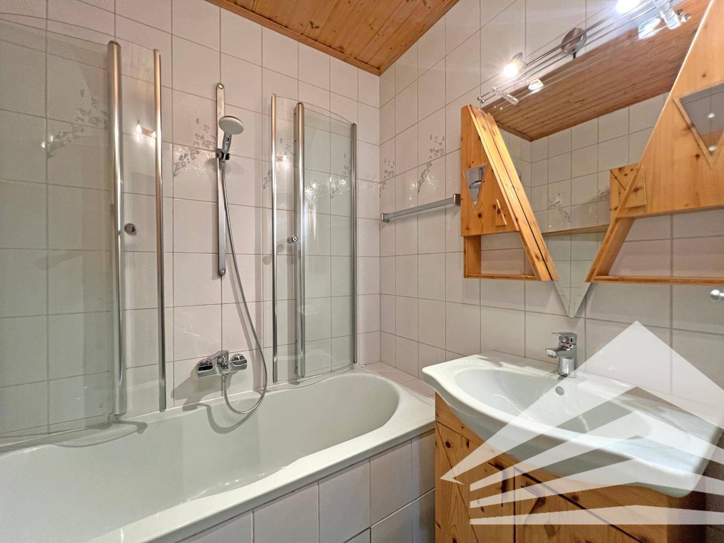 Badezimmer mit Badewanne, Duschwand, Waschbecken und Holzwaschtisch.