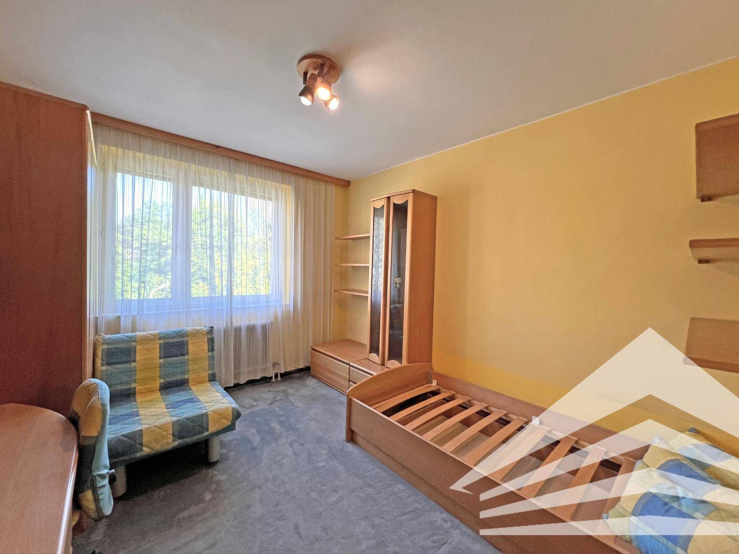 Helles Schlafzimmer mit Einzelbett, Schreibtisch und Fenster mit Blick ins Grüne.