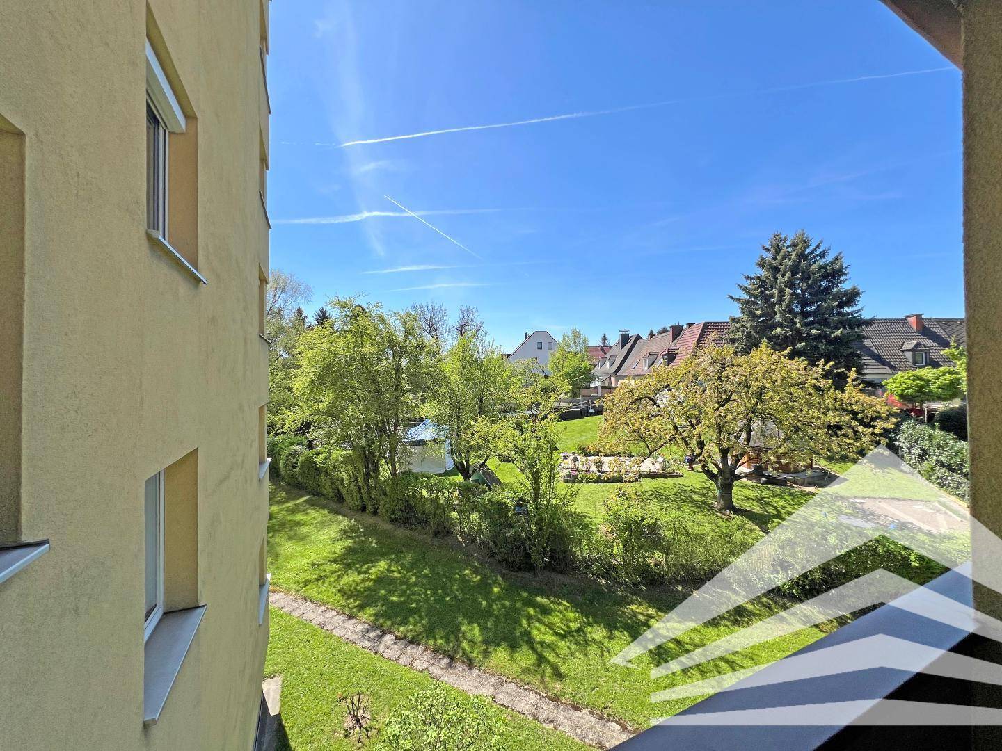Weiter Blick vom Balkon über eine gepflegte Grünfläche und Nachbarhäuser.