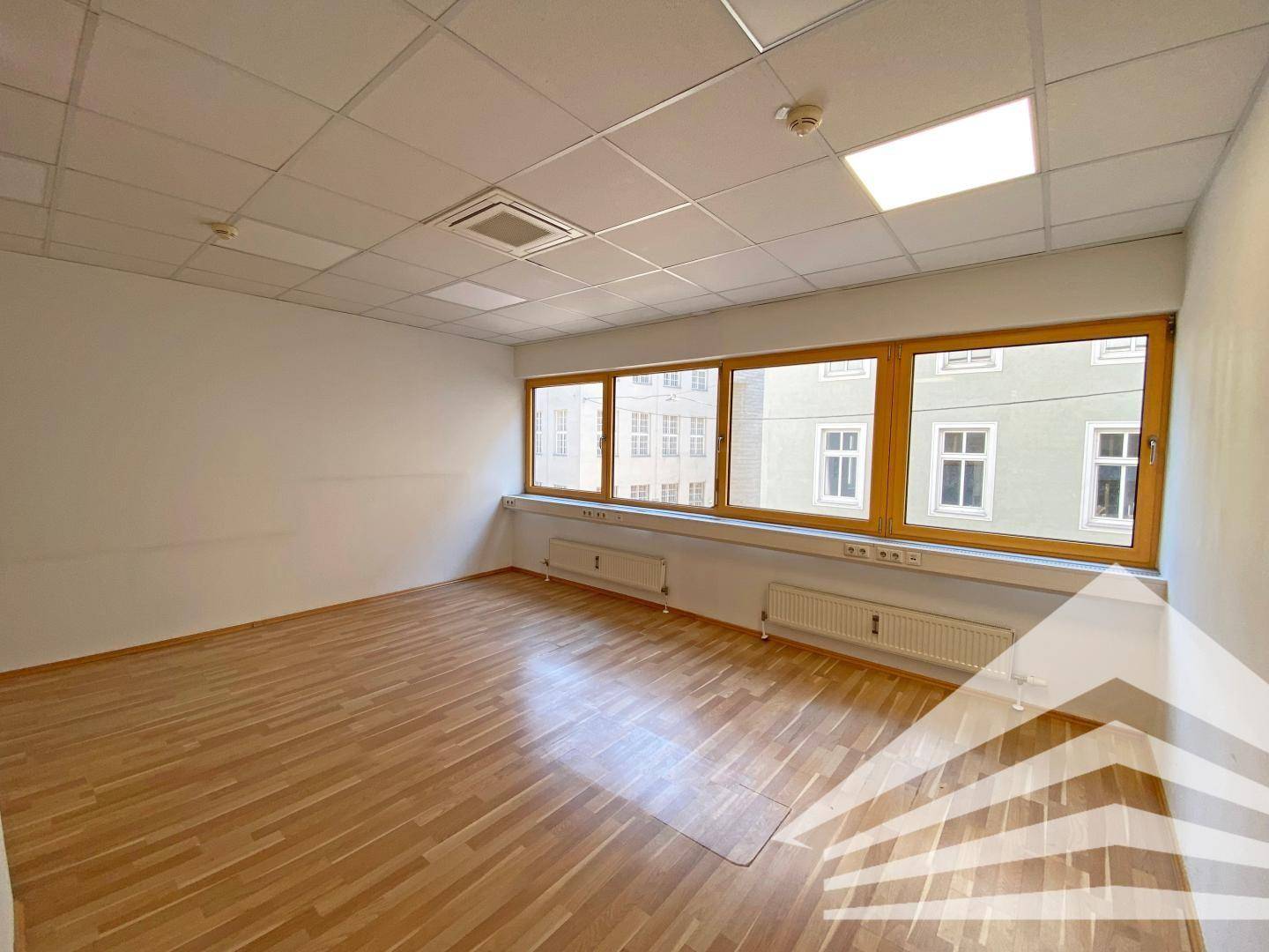 Ruhiges Büro mit großen Fenstern, Hartholzfußboden und Deckenbeleuchtung.