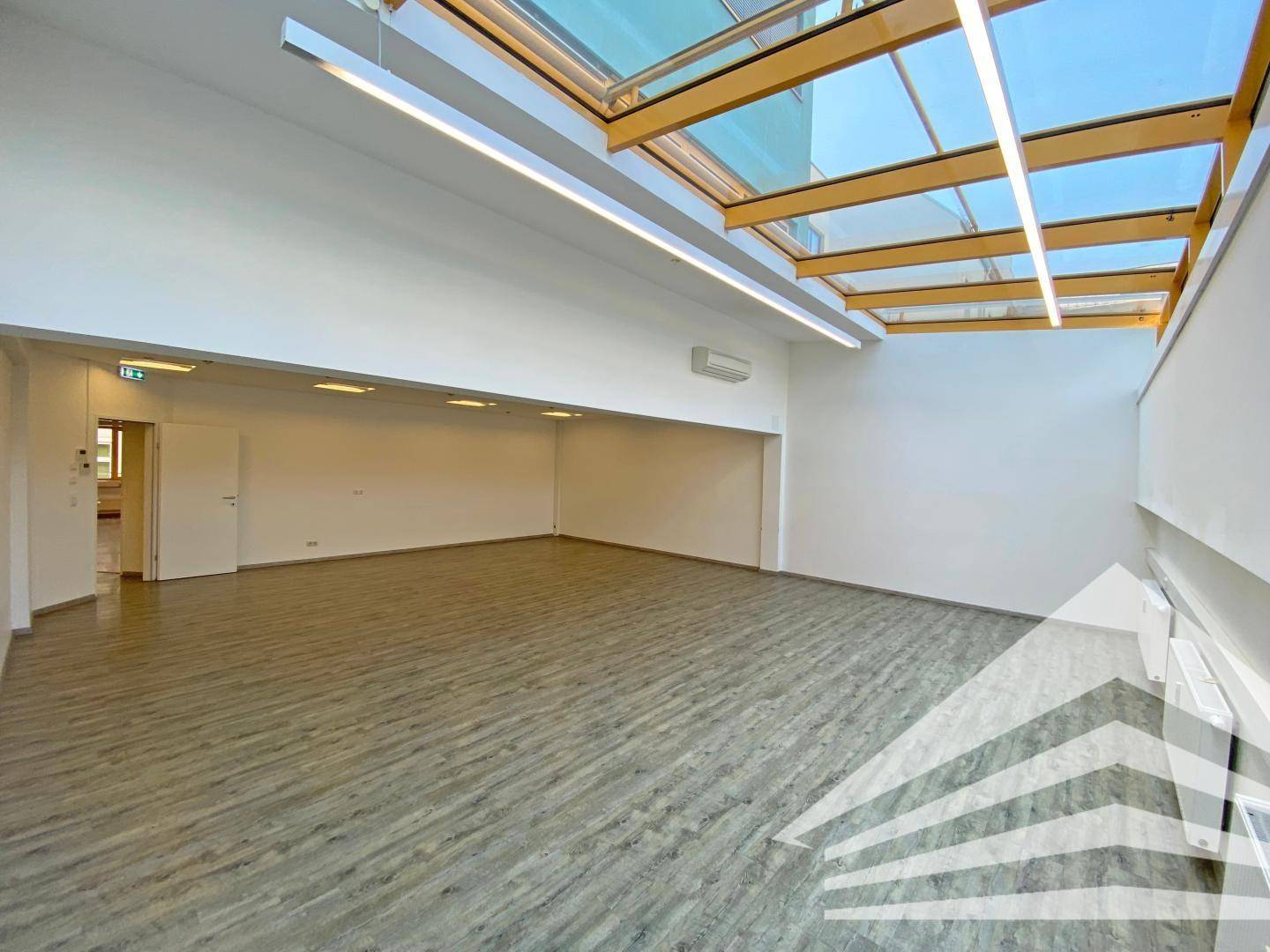 Heller Büroraum mit Glasdach, Holzbalken und moderner Deckenbeleuchtung.