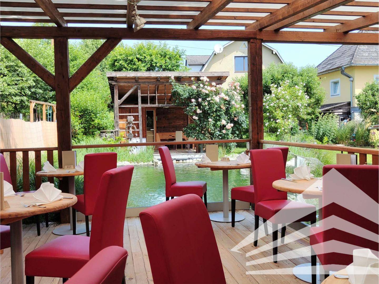Überdachte Terrasse mit roten Stühlen und Tischen, die einen schönen Blick auf den Schwimmteich bietet.