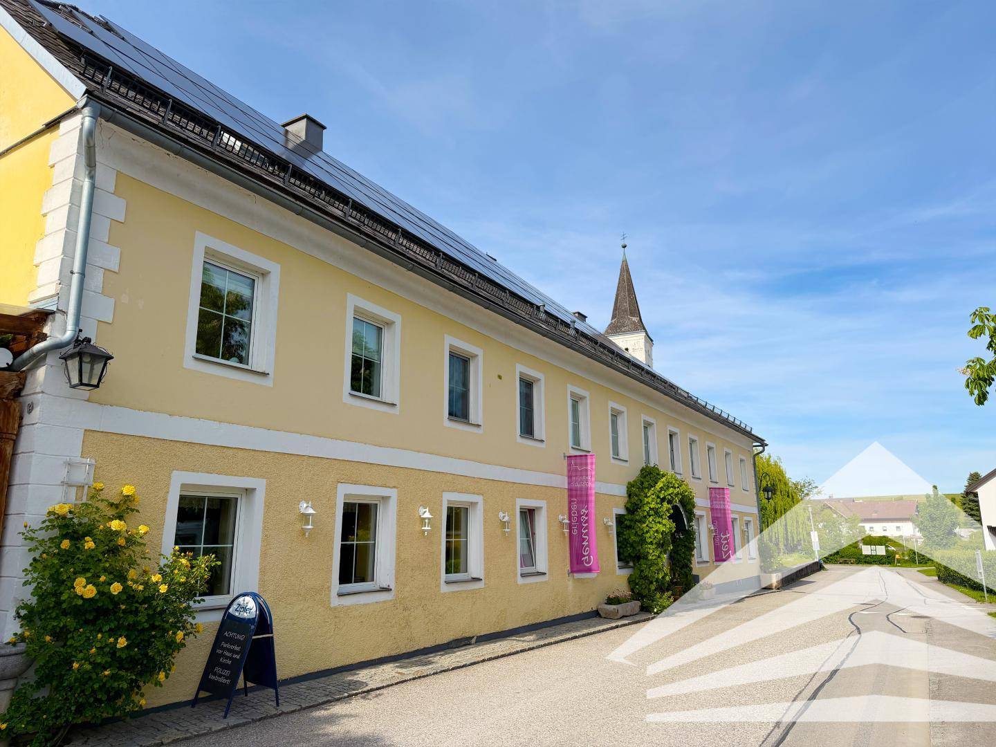 Seitenansicht des gelben Gebäudes mit Solarpaneelen auf dem Dach und einer Straße, die zum Horizont führt.