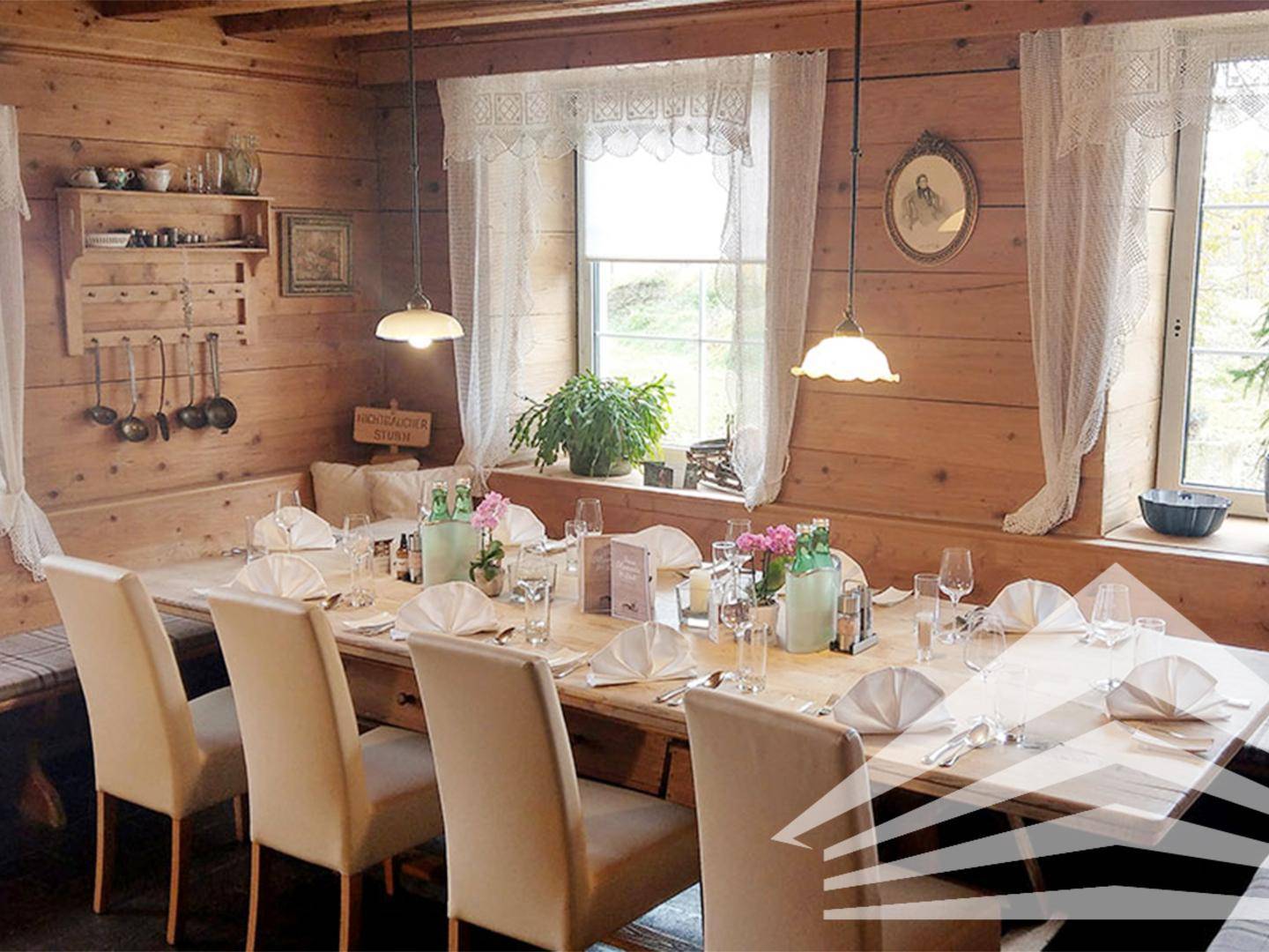 Gemütlicher Speisebereich mit Holzwänden, großen Fenstern und einem langen Tisch für gesellige Runden.