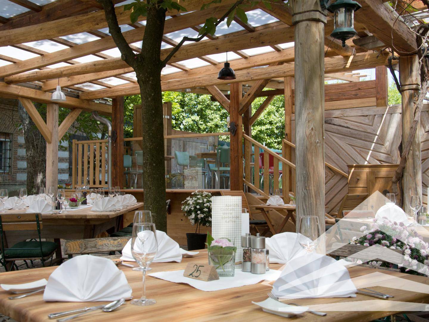 Detailansicht eines gedeckten Tisches auf der Terrasse unter einer Holzpergola mit natürlicher Bepflanzung.