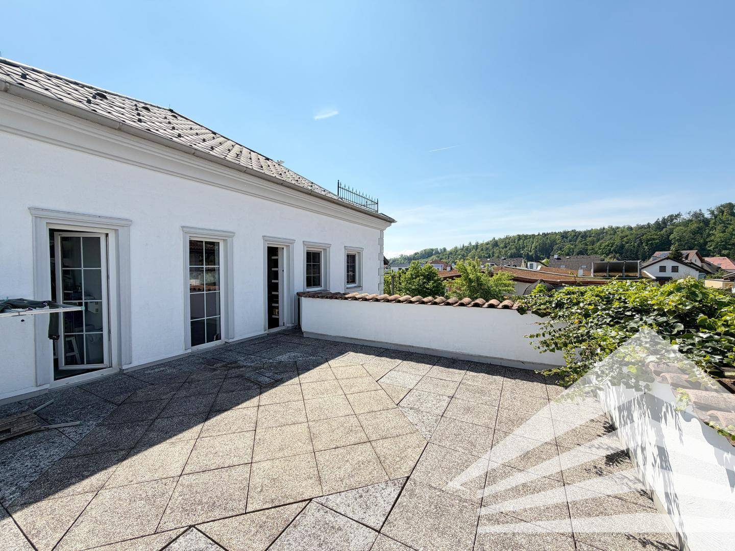Große, sonnige Terrasse mit Fliesenboden und weitem Blick über die grüne Umgebung.