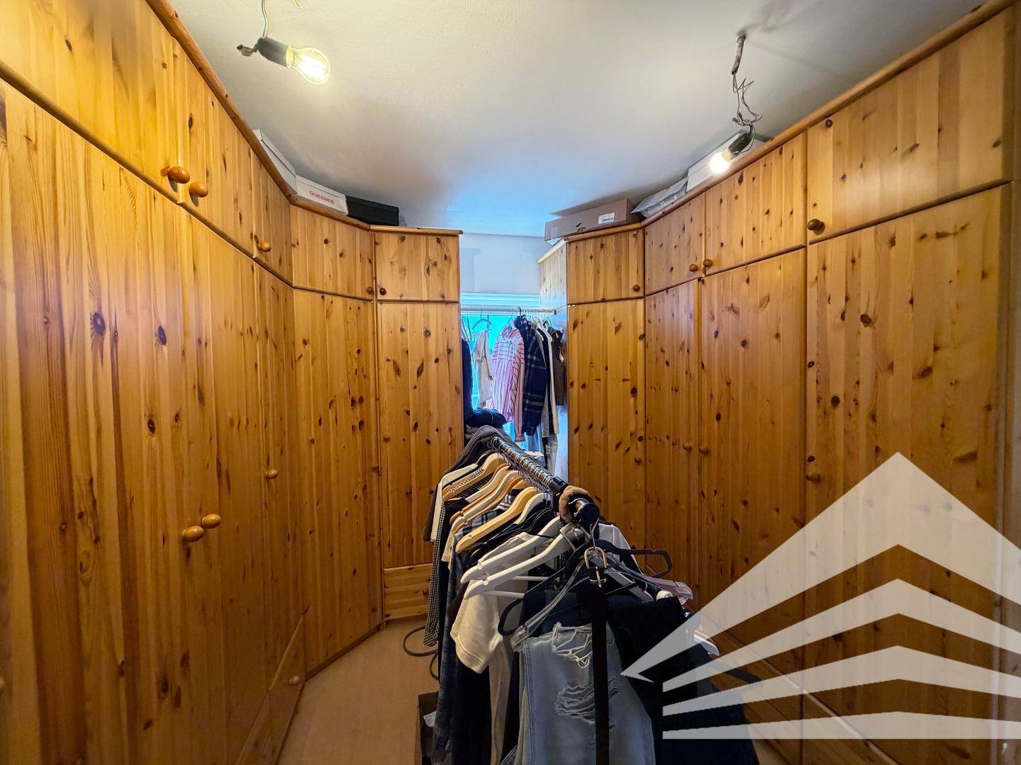 Geräumiger begehbarer Kleiderschrank mit vielen Holzschränken und Kleiderstangen für viel Stauraum.