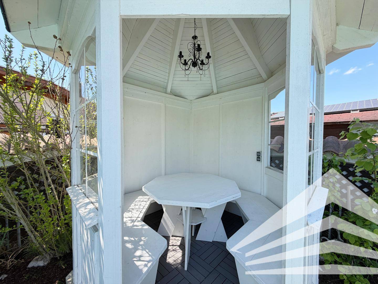 Weißer Gartenpavillon mit sechseckigem Tisch und Bänken, perfekt für gesellige Stunden im Freien.