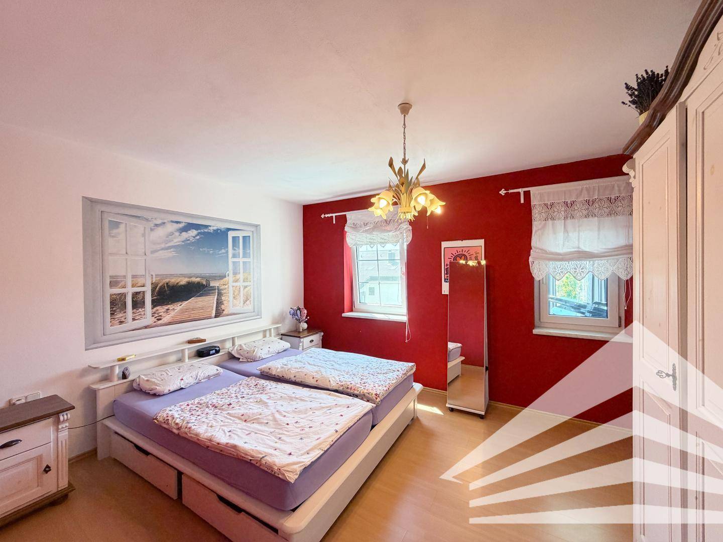 Schlafzimmer mit roter Akzentwand, zwei Einzelbetten, Holzfußboden und dekorativem Wandbild.