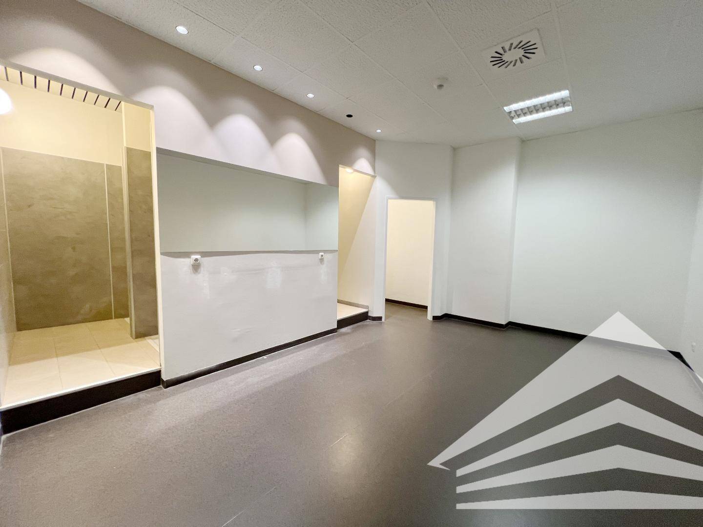 Innenansicht eines Umkleidebereichs oder Duschraums mit gefliesten Wänden und dunklem Boden in einem Gewerbeobjekt.