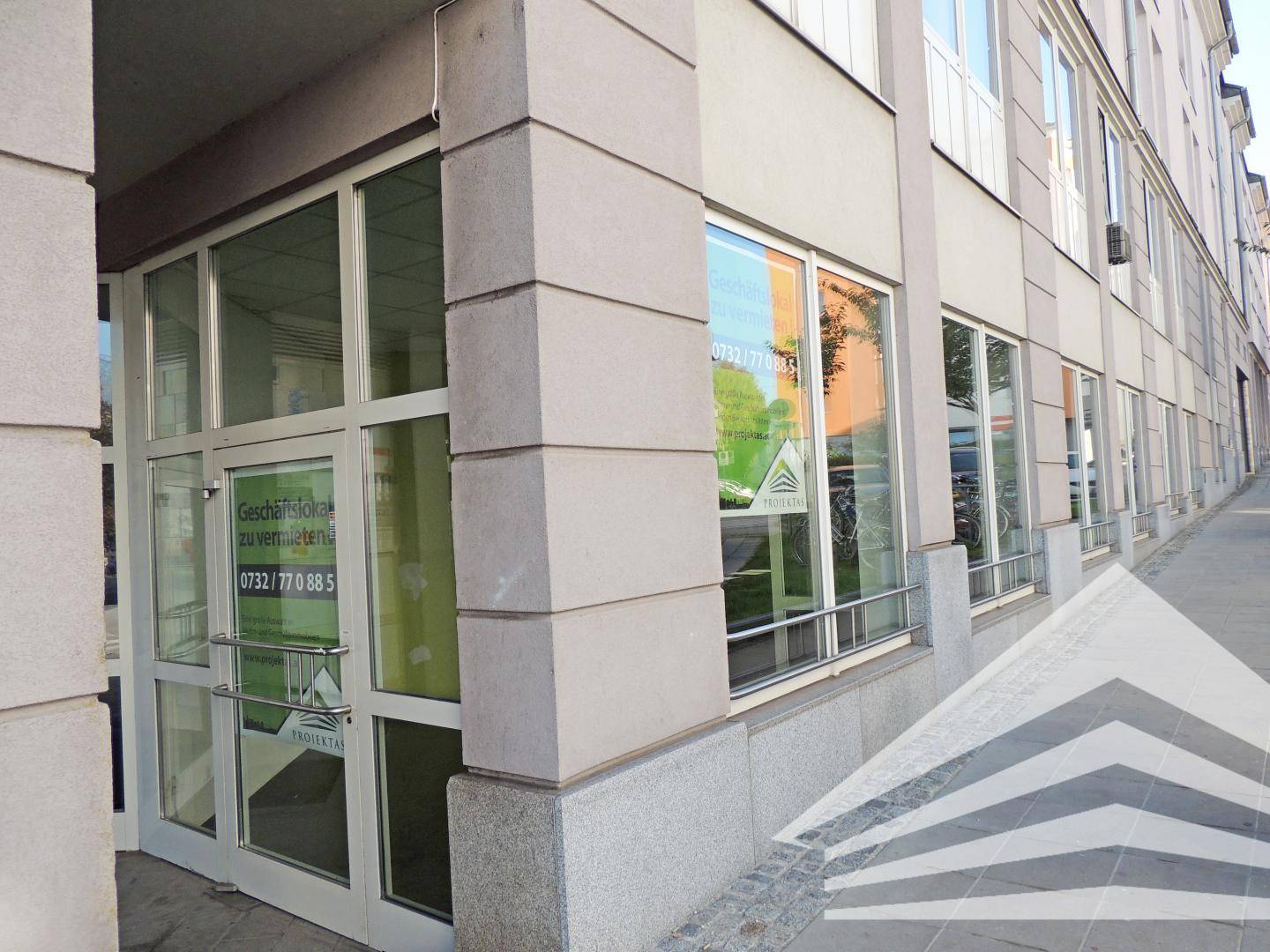 Eingangsbereich eines Geschäftsgebäudes mit großen Glasfenstern und einer modernen Steinfassade an einer Straße.