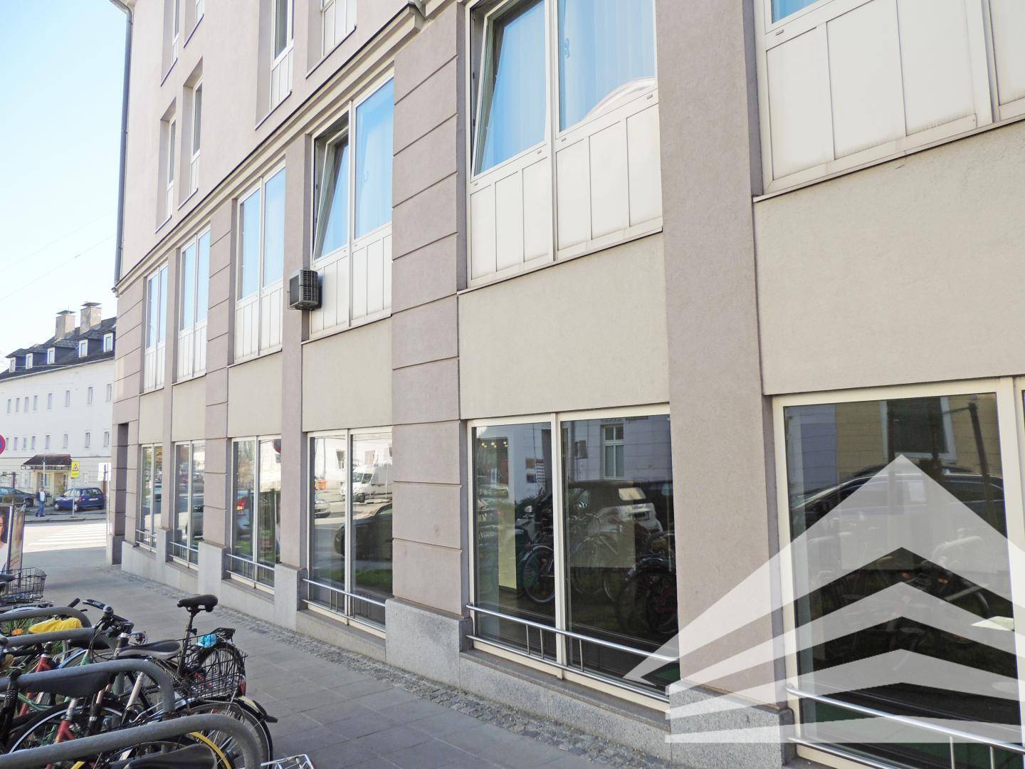 Fassade eines modernen Geschäftsgebäudes mit vielen Fenstern und Fahrradständern entlang der Straße.