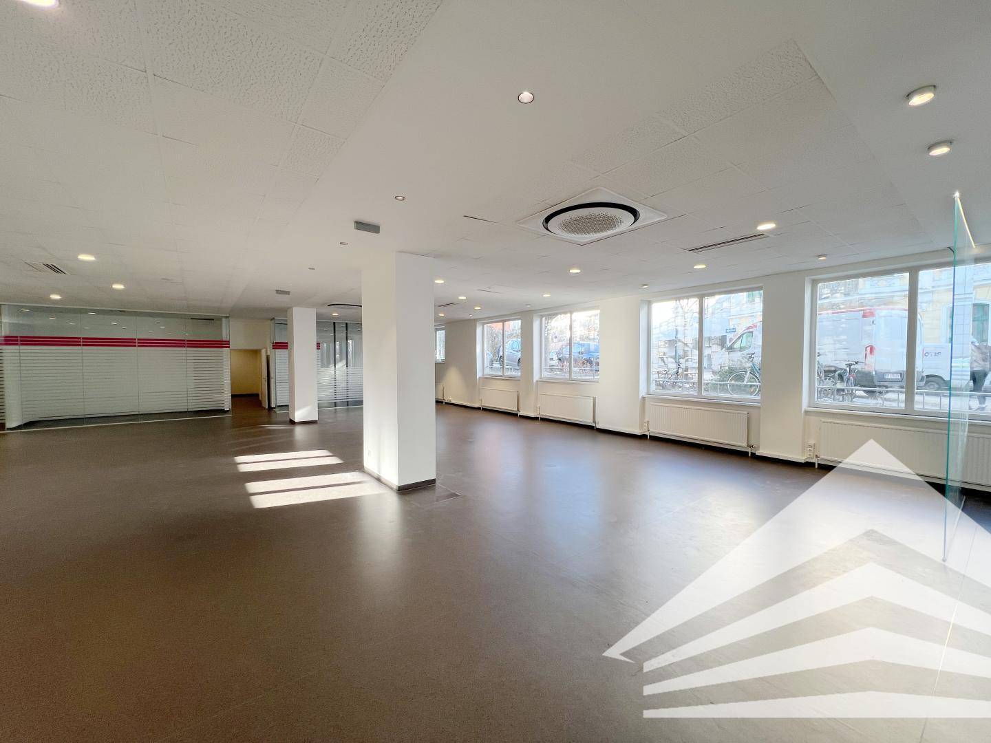 Großer, heller Gewerberaum mit vielen Fenstern zur Straße, dunklem Boden und Heizkörpern, ideal für Ladenflächen.