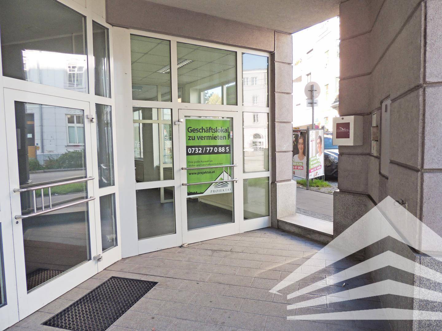 Hauptzugang eines Geschäftsgebäudes mit großen Glastüren und einem "Zu vermieten"-Schild, direkt an der Straße gelegen.