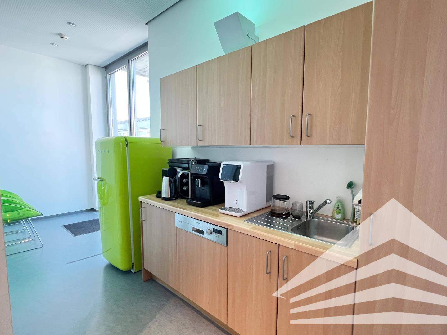 Kleine Teeküche mit Holzeinbauschränken, Spülmaschine und einem auffälligen grünen Kühlschrank.