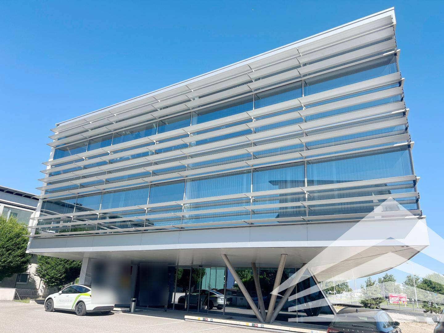 Modernes Bürogebäude mit großer Glasfassade und horizontalen Sonnenschutzlamellen unter blauem Himmel.