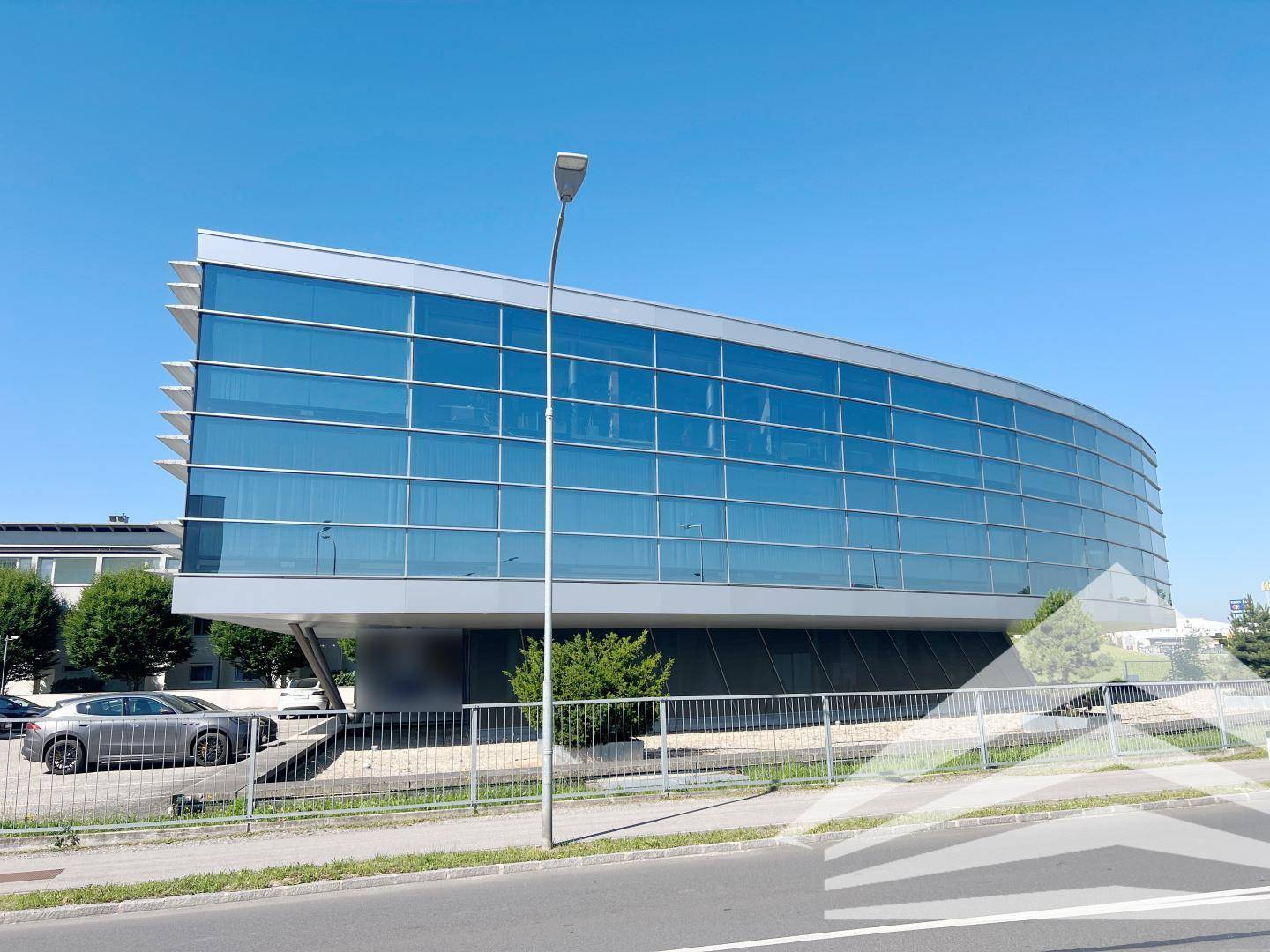 Elegantes Bürogebäude mit geschwungener Glasfassade und moderner Architektur unter strahlend blauem Himmel.