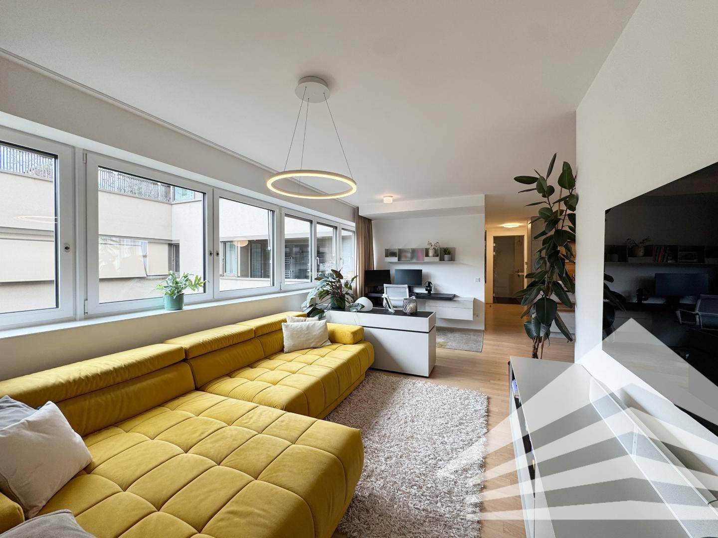 Geräumiges Wohnzimmer mit großem gelbem Sofa, Holzboden und viel Tageslicht.