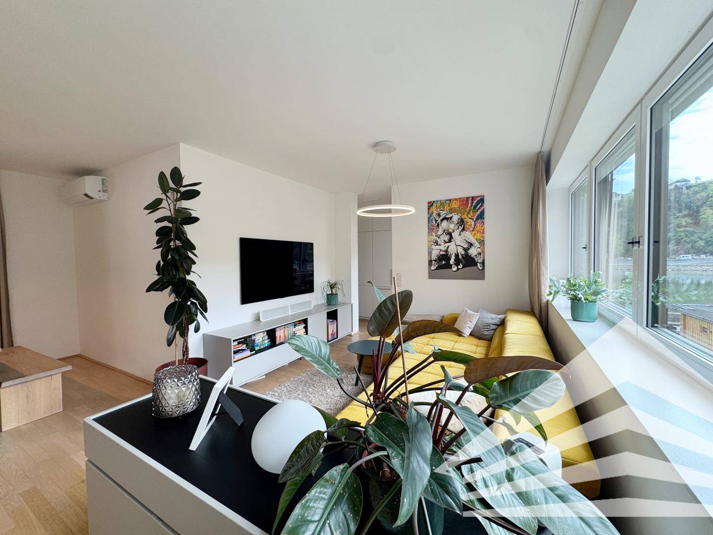 Helles Wohnzimmer mit gelbem Sofa, Fernseher und Pflanzen, bietet einen angenehmen Wohnbereich.
