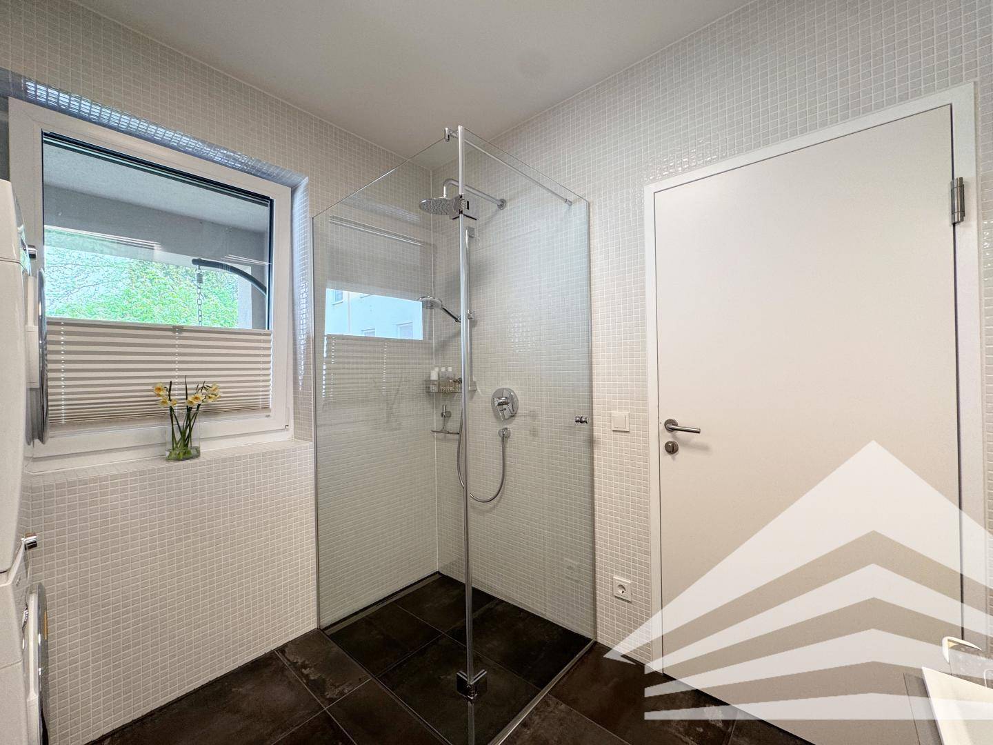 Modernes Badezimmer mit großer Duschkabine, Fenster und dunklem Fliesenboden.