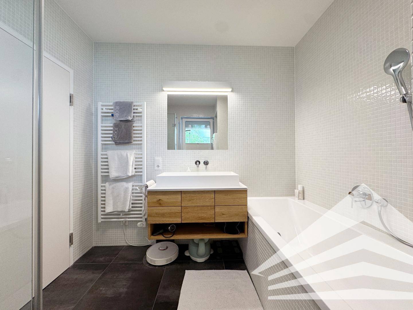 Helles Badezimmer mit modernem Waschtisch, Badewanne und beheiztem Handtuchhalter.