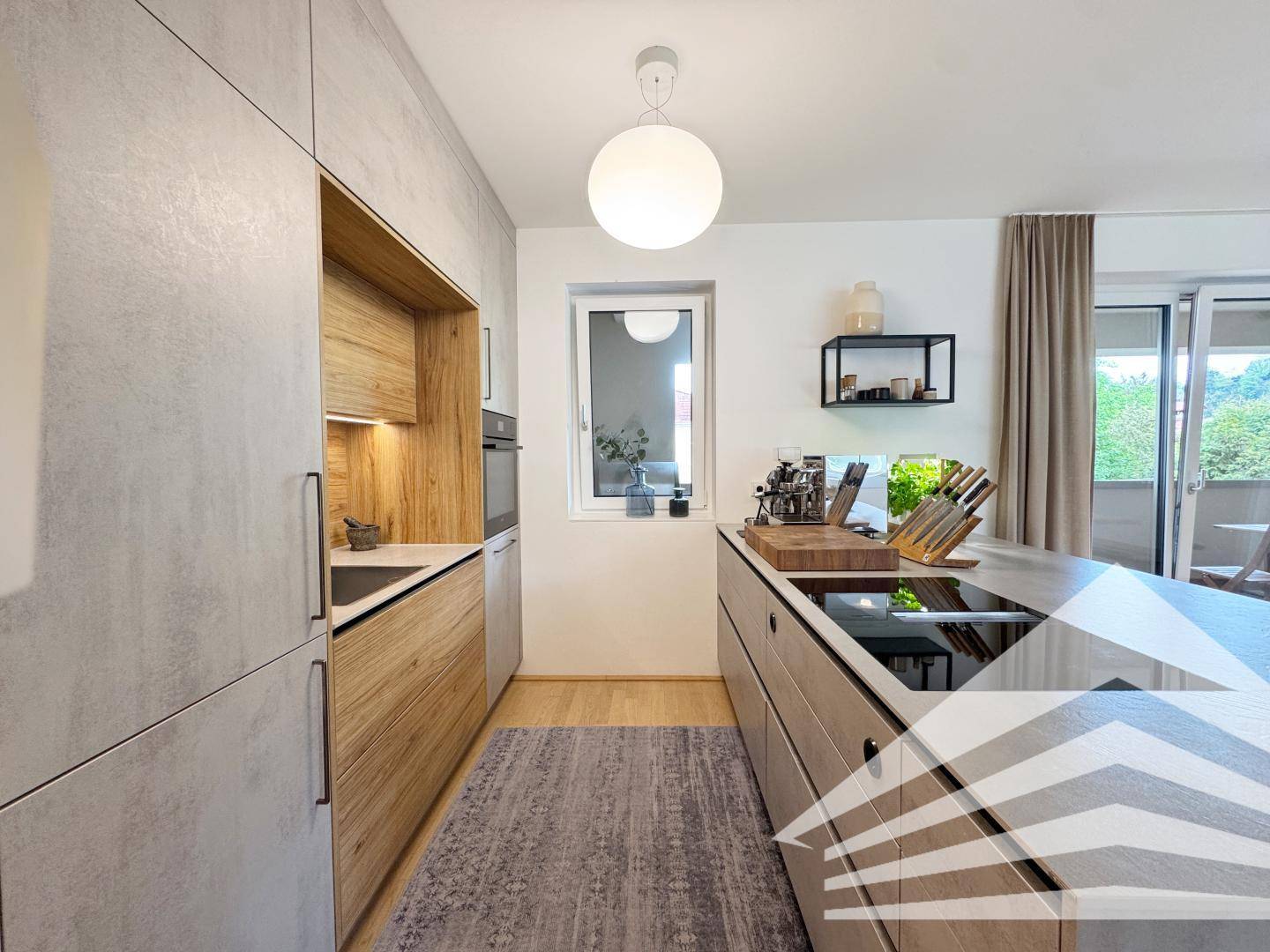 Gut ausgestattete moderne Küche mit Induktionskochfeld, Backofen und Zugang zum Balkon.