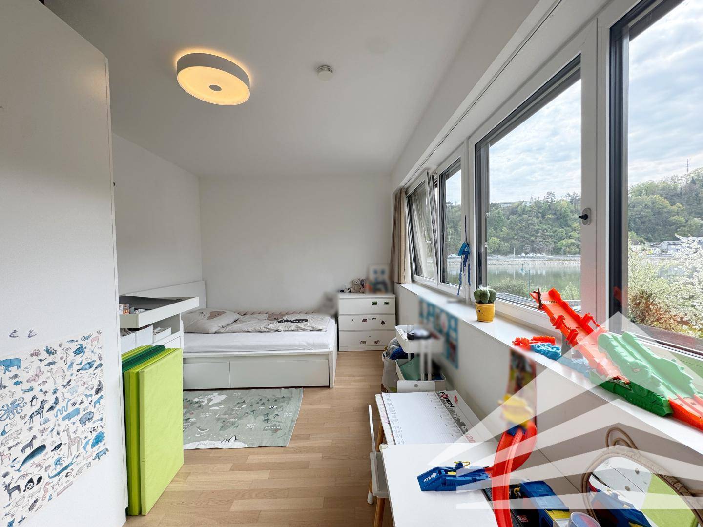 Kinderzimmer mit Bett, Schreibtisch und großen Fenstern mit Blick ins Grüne.