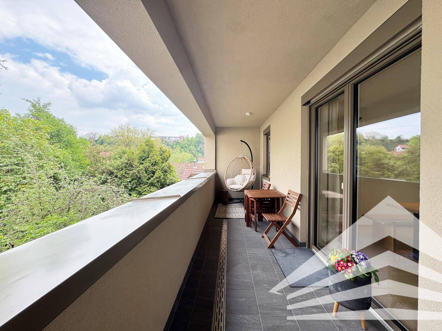 Langer Balkon mit Fliesenboden, Sitzgelegenheiten und Blick ins Grüne.