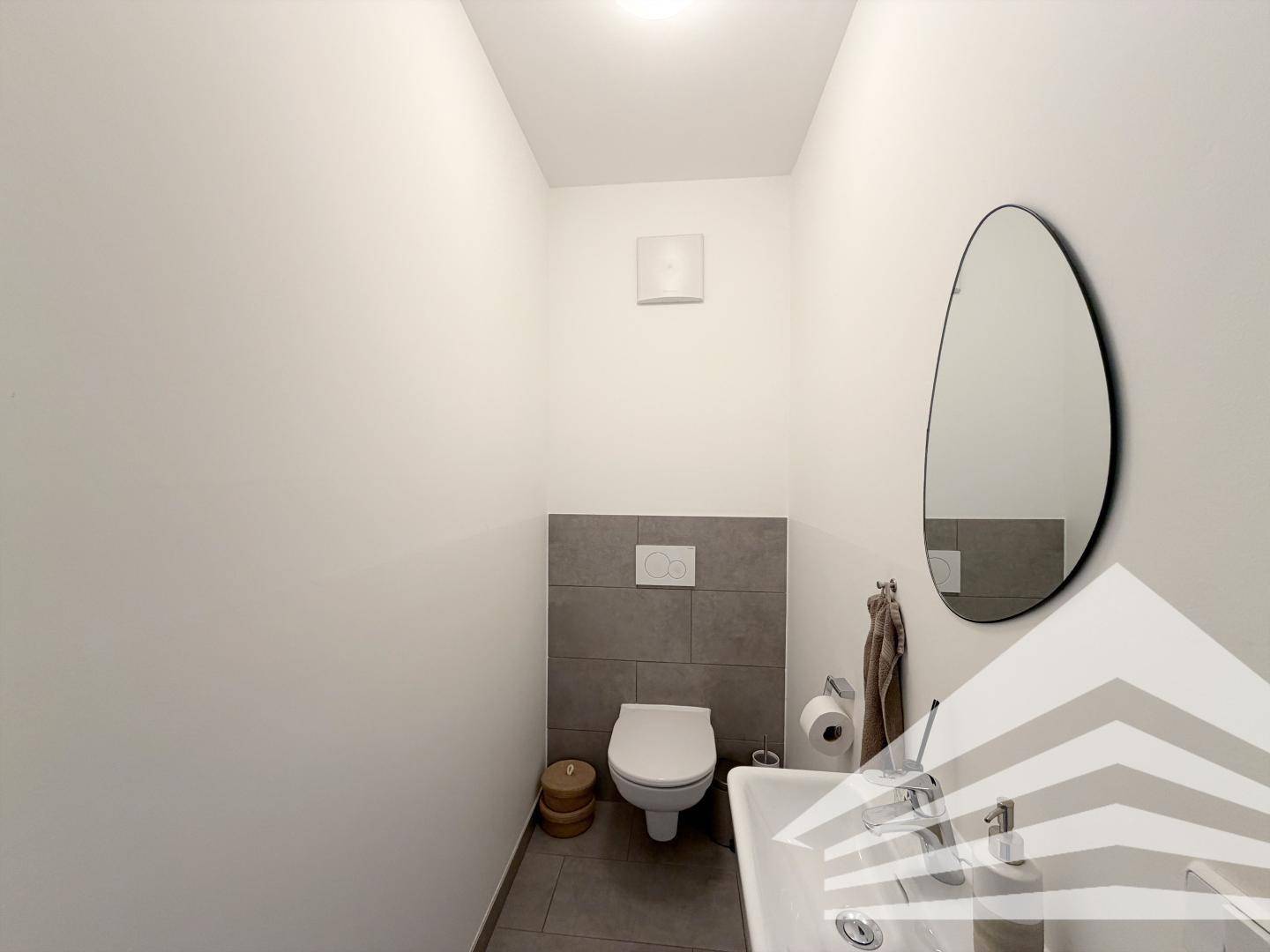 Separates Gäste-WC mit wandhängender Toilette und kleinem Waschbecken, modern gefliest.