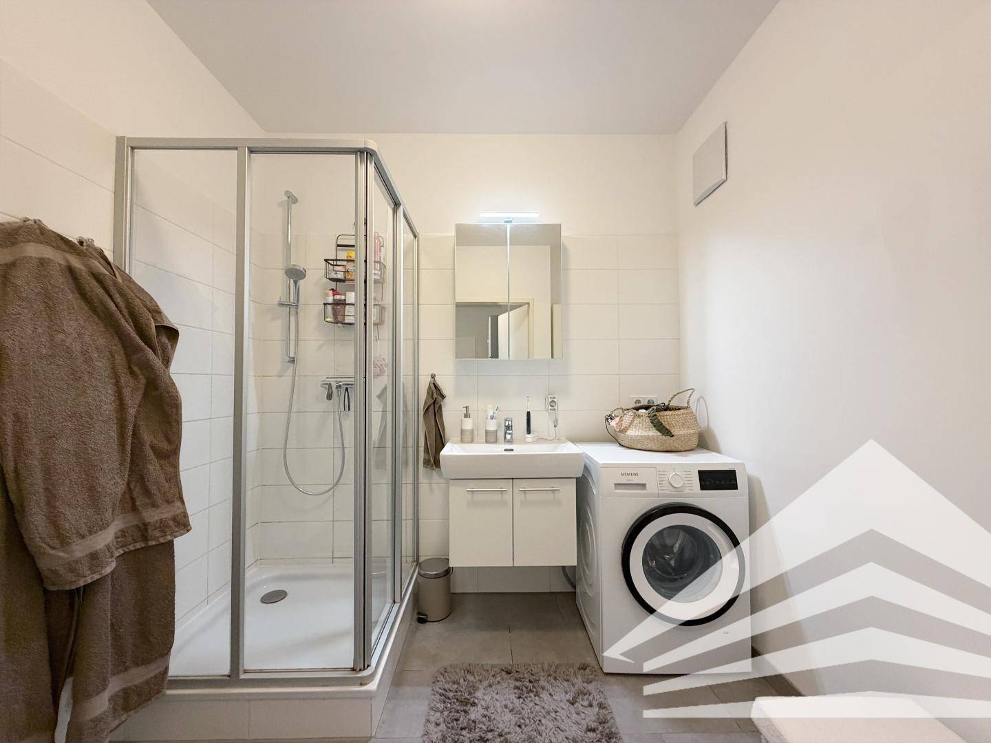 Modernes Badezimmer mit Duschkabine, Waschbecken und integrierter Waschmaschine.
