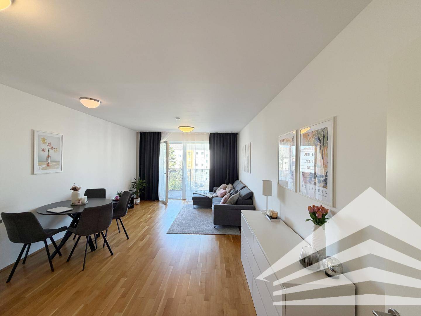 Lichtdurchfluteter Wohn-Essbereich mit Holzboden und Zugang zum Balkon durch große Fenster.