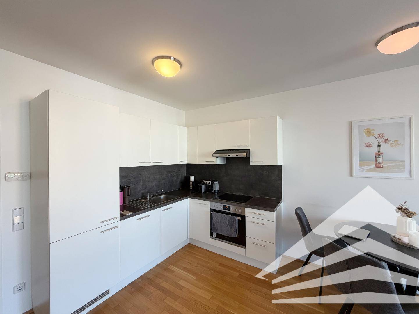 Moderne Einbauküche mit weißen Schränken, dunkler Arbeitsplatte und integrierten Geräten.