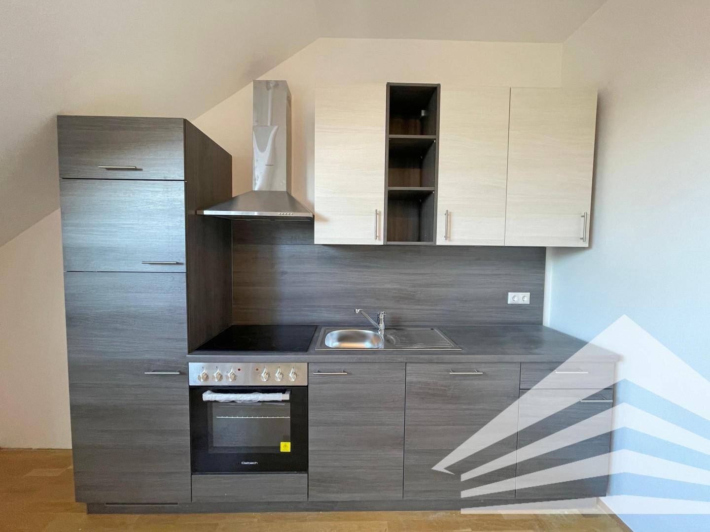 Moderne Küchenzeile im Dachgeschoss mit grauen Unterschränken, hellen Oberschränken und integrierten Geräten.