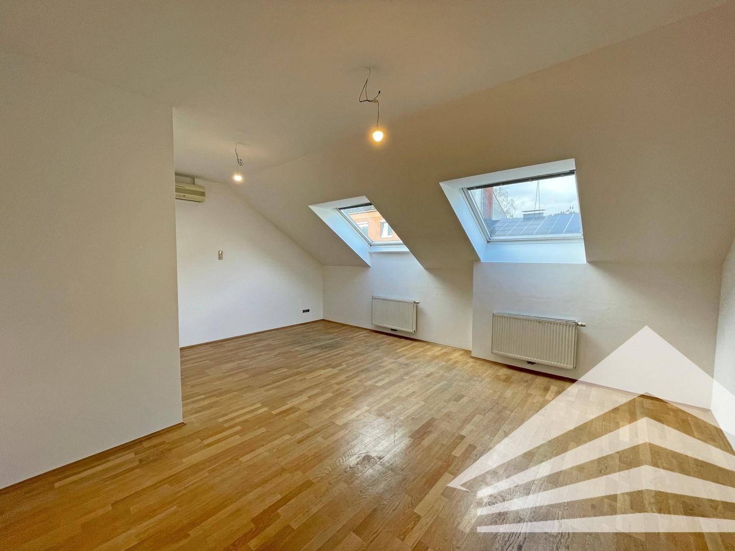Geräumiger Dachgeschossraum mit Holzboden, zwei Dachfenstern und viel natürlichem Licht.