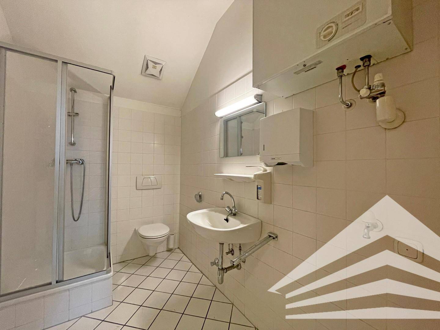 Funktionales Badezimmer mit Dusche, WC, Waschbecken und weißen Fliesen im Dachgeschoss.