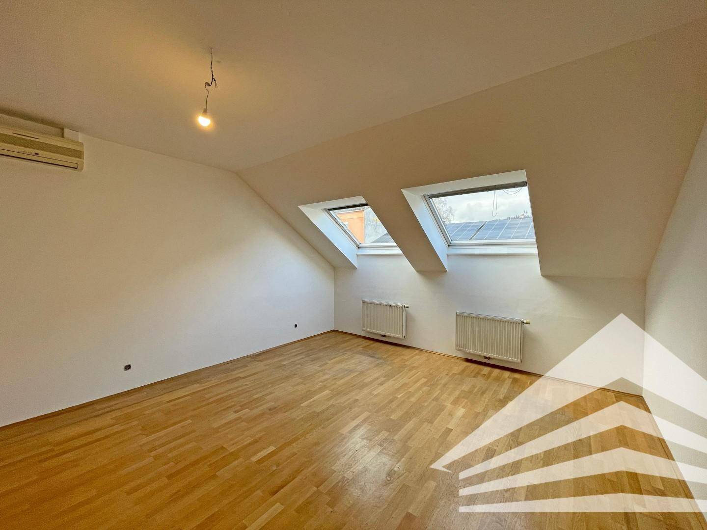 Lichtdurchfluteter Dachgeschossraum mit Holzboden, schrägen Wänden und zwei Dachfenstern.