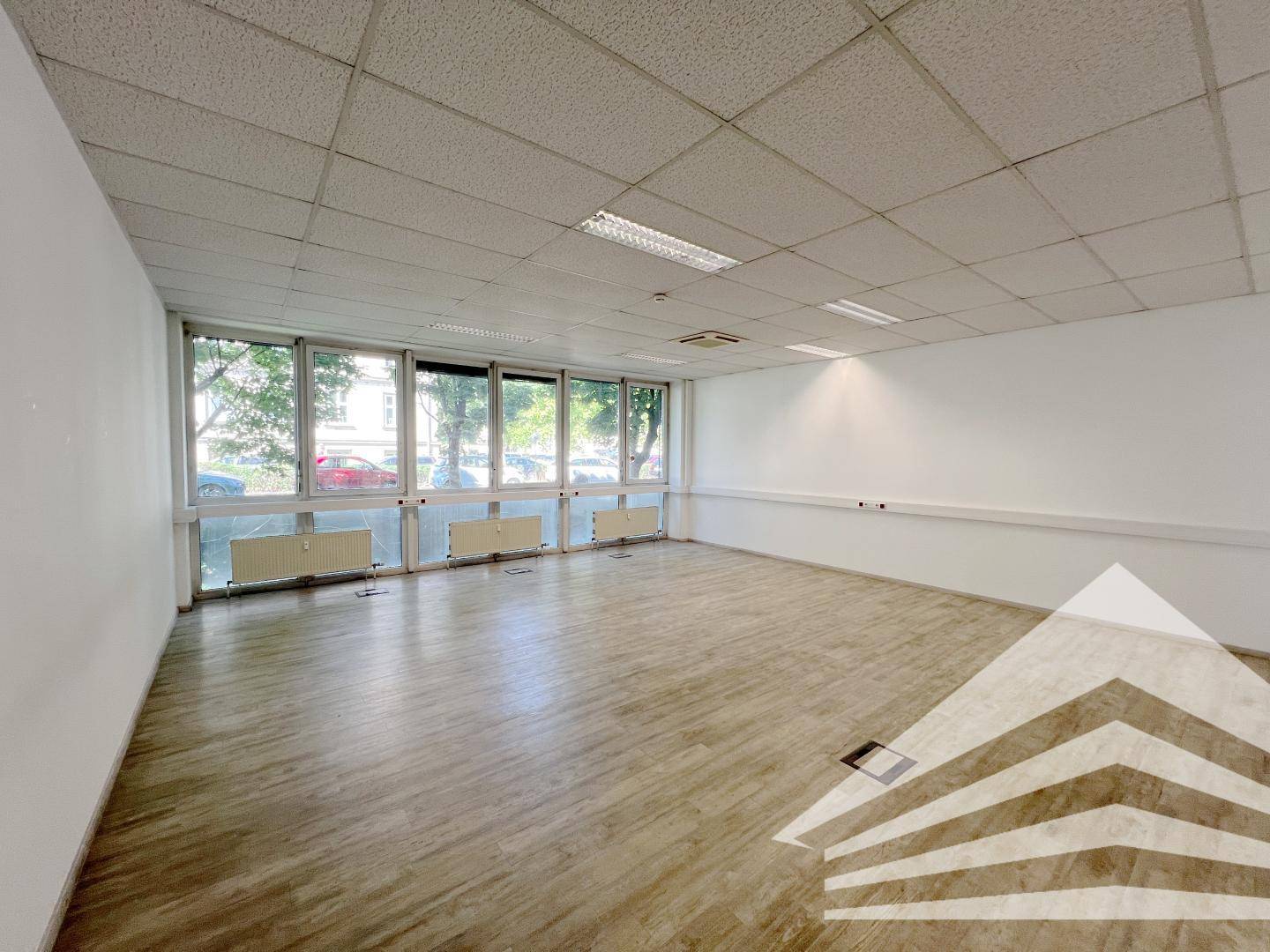 Weitläufiges Büro mit heller Laminatboden und großen Fenstern, die einen Blick nach draußen ermöglichen.
