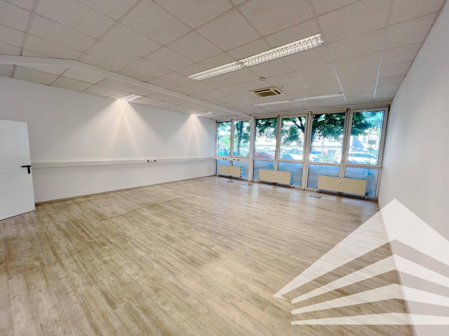 Helles und geräumiges Büro mit Laminatboden und einer Reihe von Fenstern, die viel Tageslicht hereinlassen.