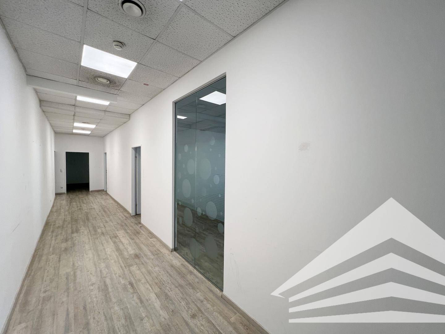 Heller Flur mit Laminatboden und einer modernen Glaswand, die zu einem angrenzenden Büro führt.