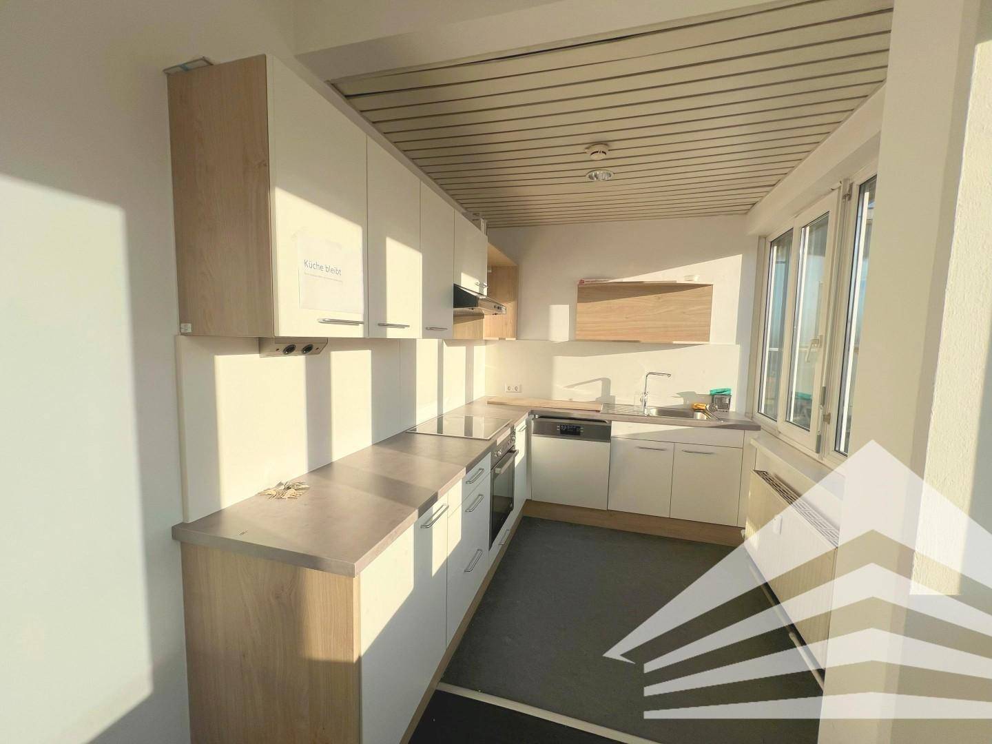 Moderne Teeküche mit hellen Holz- und weißen Schränken, Spüle und integriertem Geschirrspüler.