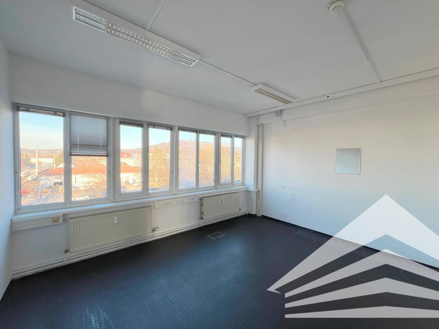 Leerer Büroraum mit breiter Fensterfront, dunklem Boden und Heizkörpern unter den Fenstern.