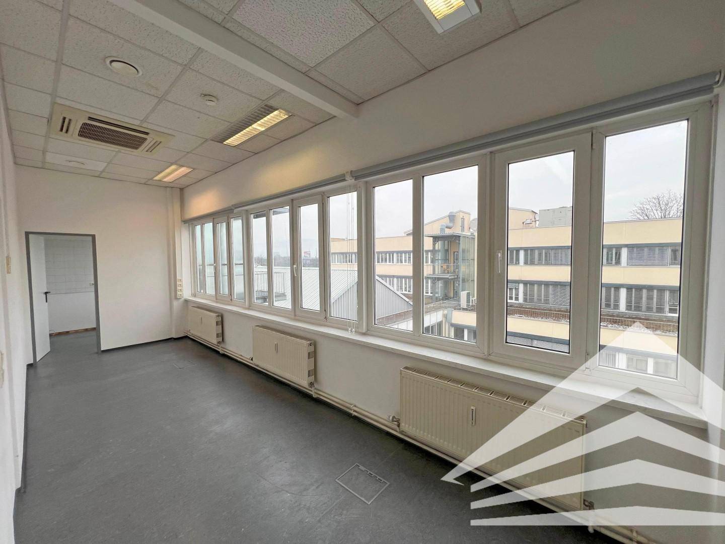 Geräumiges Büro mit langer Fensterfront, grauen Bodenfliesen und abgehängter Decke, bietet Weitblick.