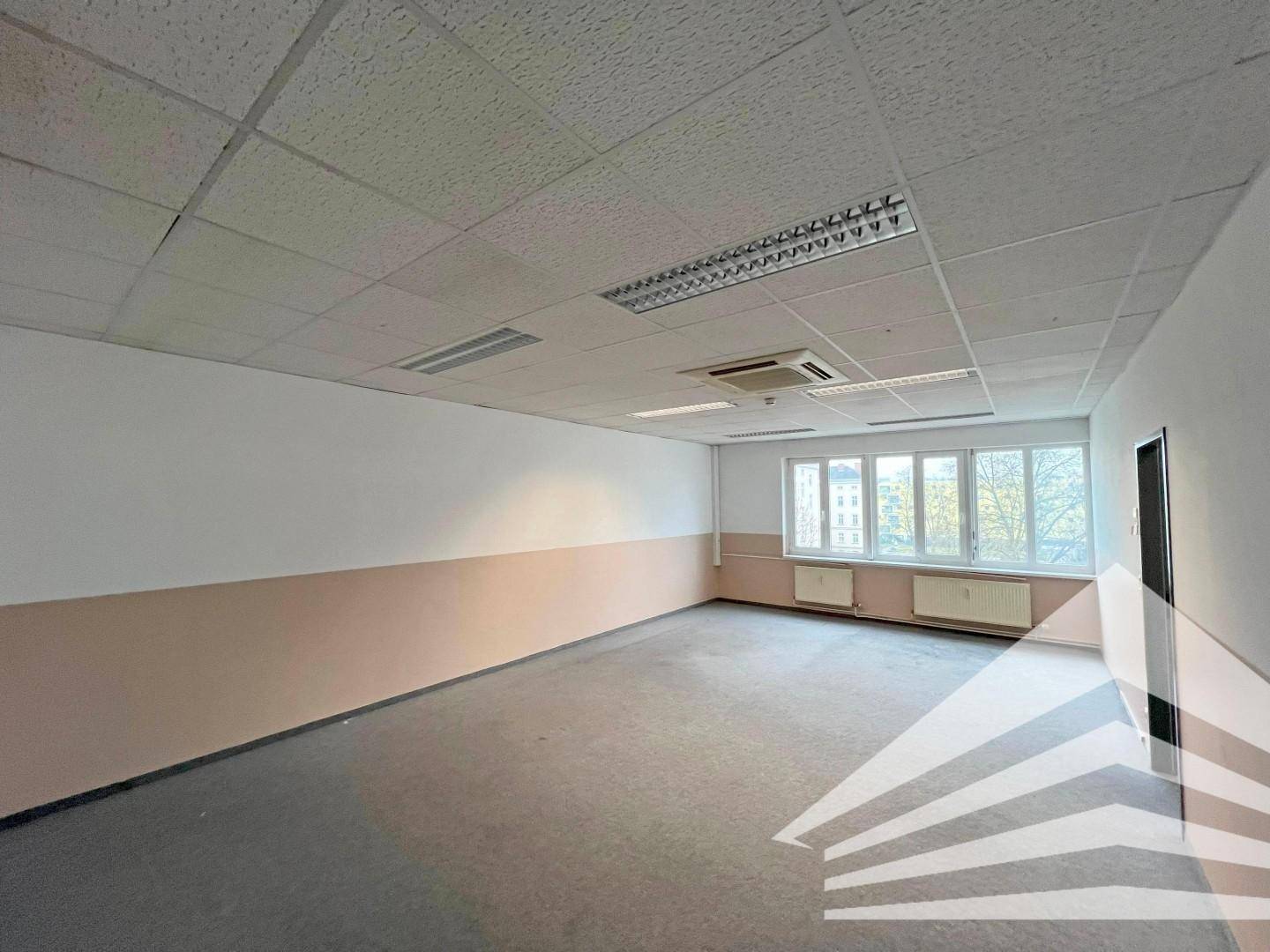 Leeres Büro mit dunklem Teppichboden, abgehängter Decke und Fenstern, bereit für die individuelle Gestaltung.