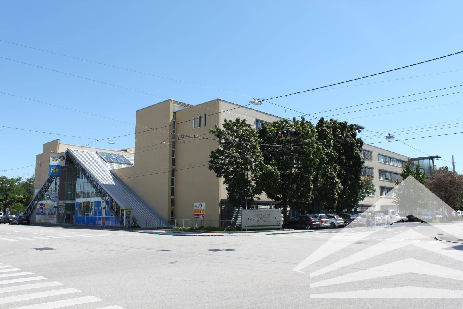 Modernes Bürogebäude an einer Straßenecke mit markanter Architektur und vielen Fenstern, unter blauem Himmel.