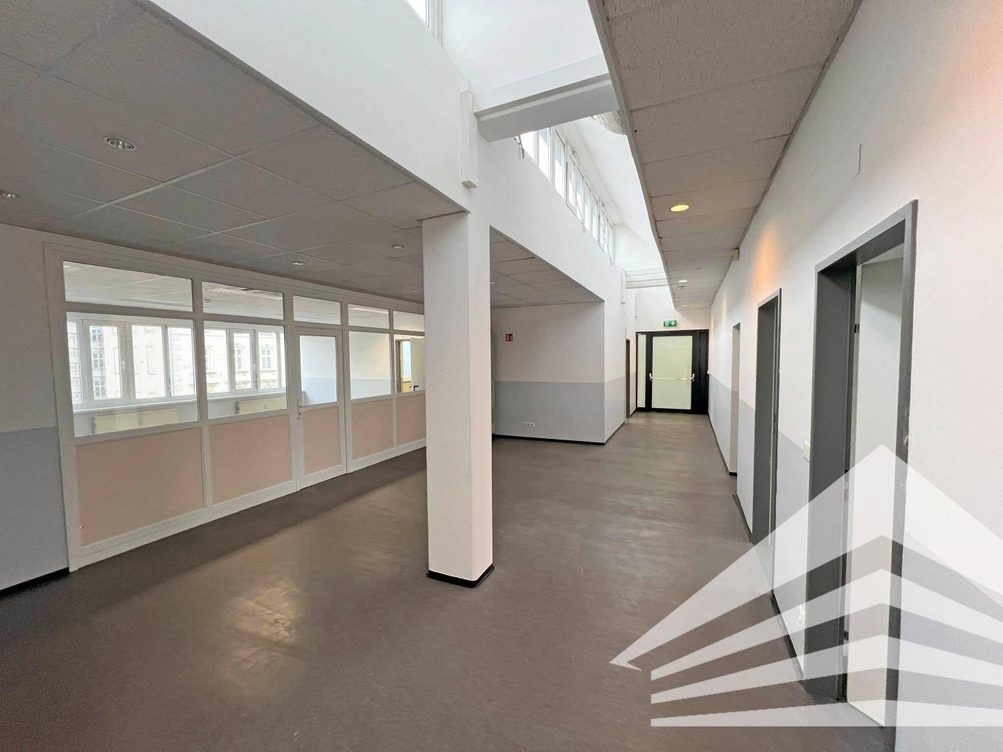 Langer Bürogang mit Glasabtrennungen zu den Seiten und mehreren Türen, ausgestattet mit abgehängter Decke.